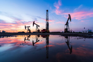 in the evening, oil pumps are running, The oil pump and the beautiful sunset reflected in the water, the silhouette of the beam pumping unit in the evening.