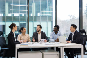 Diverse business colleagues and partners sitting at tables in meeting room, people happily discussing new startup and business investment, company employees with boss in business suit
