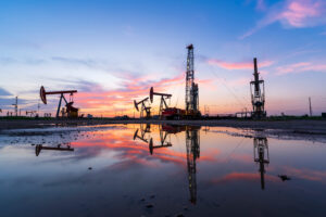 in the evening, oil pumps are running, The oil pump and the beautiful sunset reflected in the water, the silhouette of the beam pumping unit in the evening.