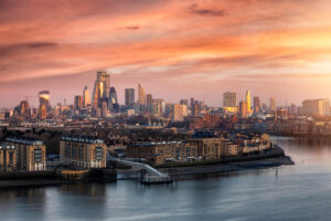 The urban skyline of London, United Kingdom, along the Thames river to the City during a colorful sunrise with orange and pink cloudscape